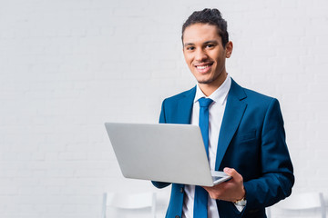 Wall Mural - Smiling businessman holding laptop on white wall background