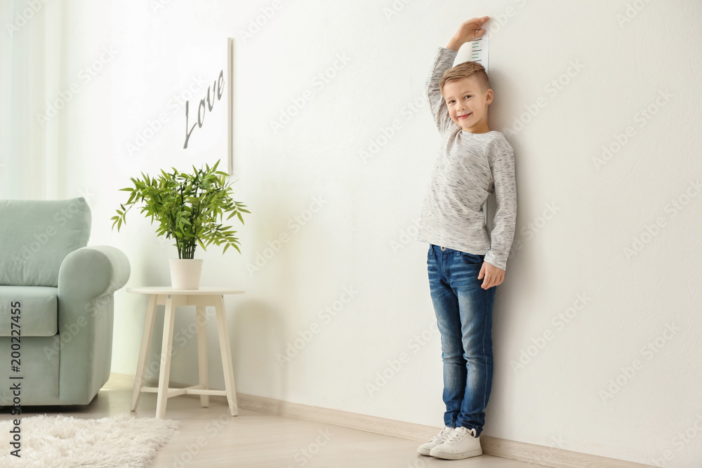 Cute little boy measuring height near wall at home