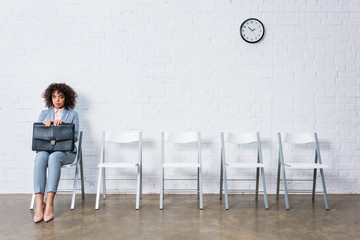 Confident businesswoman with briefcase sitting on chair and waiting