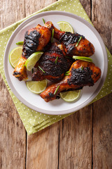 Canvas Print - Caribbean grilled chicken drumstick with lime and onions closeup on a plate. Vertical top view from above