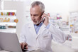 Business call. Senior attentive male pharmacist working on laptop while calling