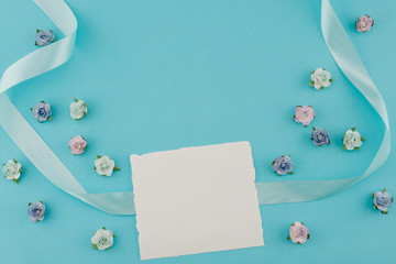 White blank card decorate with blue tone paper flowers and ribbon on pastel blue background with copy space