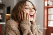 © Drobot Dean - Portrait closeup of astonished woman in knitted sweater, sitting at table in coffee shop and looking through window with amazement