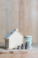 Wooden house piggy bank with dollar money and coin on wooden table over wood background metaphor saving money for buy home and real estate