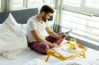 © BGStock72 - Man eating breakfast in bed whilst using mobile phone