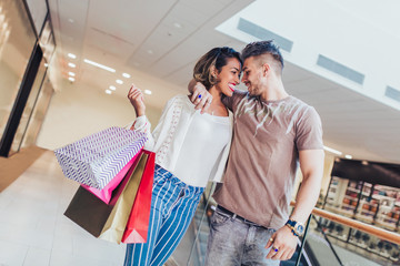 happy young couple with shopping bags walking in mall - sale, consumerism and people concept