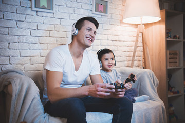 Father and son are playing video games on tv at night at home.