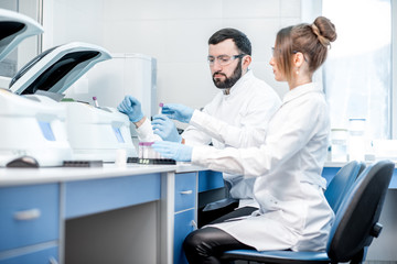 Wall Mural - Laboratory assistants making analysis with test tubes and analyzer machines sitting at the modern laboratory