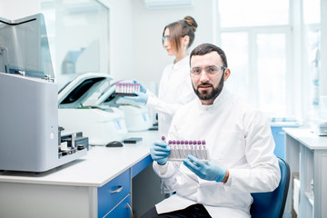 Wall Mural - Portrait of a male laboratory assistant making analysis with test tubes and analyzer machines sitting at the modern laboratory