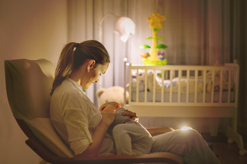 Wall Mural - Young beautiful mother, breastfeeding her newborn baby boy at night, dim light