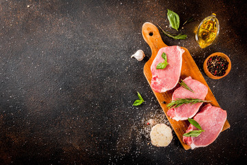 Wall Mural - Raw meat, pork steaks with spices, herbs, olive oil, dark background top view, copy space