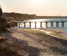 Pier In The Sea At Sunset. Promenade And Sea Pier In The Rays Of The Rising Sun. The Sea Coast After A Storm.