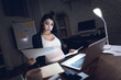 © freeograph - Tired pregnant girl examines documents behind laptop. Pregnant in dark office.
