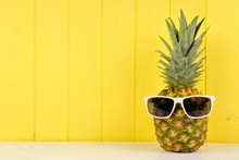 Hipster Pineapple With Trendy Sunglasses Against Yellow Wood Background. Minimal Summer Concept.