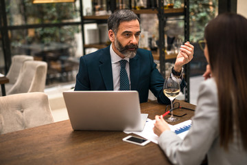 Business man sitting with his female colleague in a restaurant and talking about job while drinking wine.