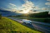 White truck driving on the highway in the countryside in the rays of the sunset with dramatic clouds