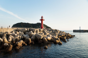 Wall Mural - Lighthouse with a watching person at the seawall with wavebreakers in Seogwipo, Jeju Island, South Korea