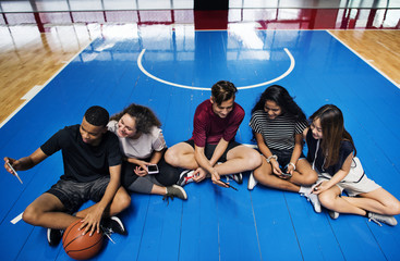group of young teenager friends on a basketball court relaxing and using smartphone