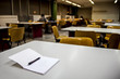 © federqua - Quaderno bianco con penna su una scrivania di una sala studio universitaria con ragazzi sullo sfondo