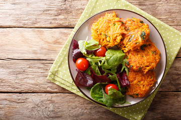 Wall Mural - Homemade fritters of sweet potatoes and fresh mix of salad on a plate macro. Horizontal top view