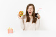 © ViDi Studio - Angry screaming woman sitting at table with burger, french fries, cola in glass bottle isolated on white background. Proper nutrition or American classic fast food. Advertising area with copy space.