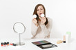 © ViDi Studio - Attractive fun woman wipes her skin face with facial sponges, sits at table applying makeup with set facial decorative cosmetics isolated on white background. Beauty female fashion lifestyle concept.