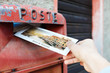© simone_n - Male hand is drops a postcard in a red postbox in Venice, Italy. The postcard shows a Venice canal.