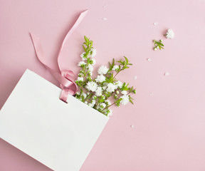 Flat lay top view White gift bag and spring flowers on a pink background. Greeting card with delicate flowers Pink floral background