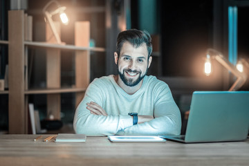 Perfect job. Gay bearded IT guy posing at table while smiling and looking at camera