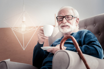 Great mood. Nice joyful positive man holding a cup of tea and smiling while being in a great mood