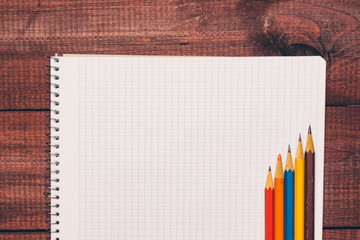 Bright used colorful pencils next to a blank sheet of paper. Work supplies stationery on a wooden texture table. Trendy minimalism. Concept of a modern freelancer workplace. Rustic cozy atmosphere