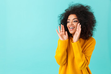 Wall Mural - Multicolor portrait of splendid curly woman in yellow shirt holding hands at face and calling or screaming near copy space, isolated over blue background