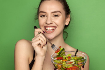 Young beautiful woman eating salad on green background