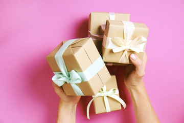 Young woman holding bunch of presents wrapped in hand made blank craft paper gift wrap, satin bow. Female hands, simple giftbox, wrapping, giftwrap, silk ribbon. Pink background, close up, copy space.