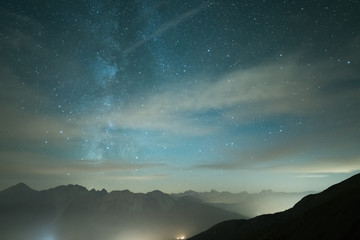 Wall Mural - milky way galaxy and starry sky from high elevation in summertime on the alps. fog and mist, city li
