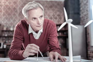 Wall Mural - Inspiring idea. Budding ambitious male engineer staring at windmill model while leaning on table and working on blueprint