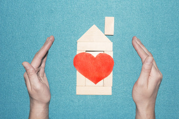 Wall Mural - concept is to protect and love the house. Protection of the home and family. Insurance of real estate. Wooden toy house of cubes with red heart inside and hands outside