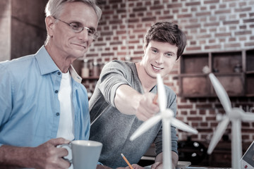 Wall Mural - Two generations. Satisfied glad male engineers staring at windmills model while working together and sharing thoughts