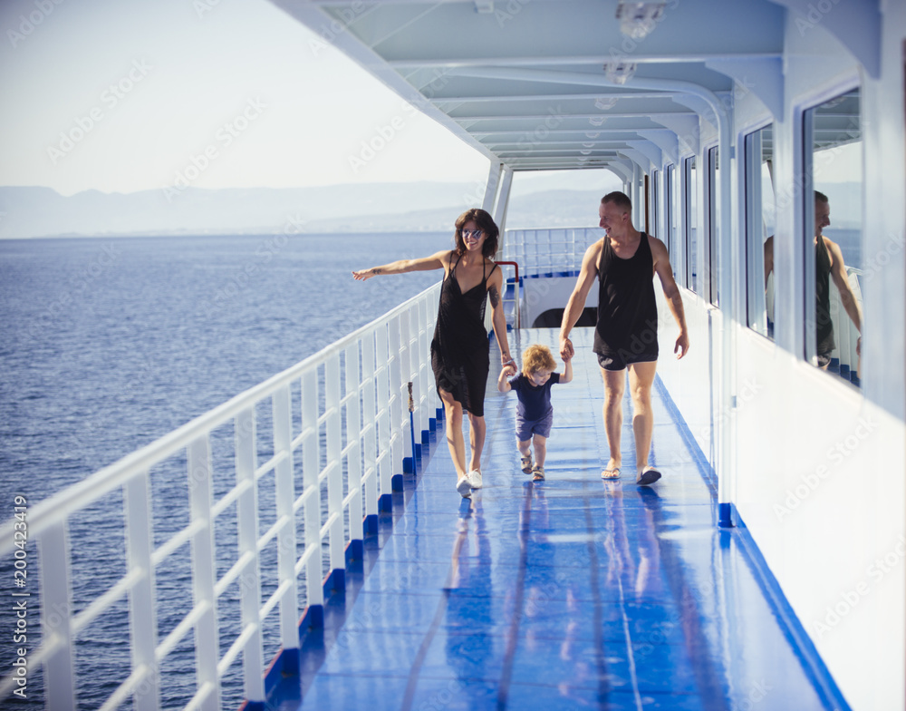 Happy family with cute son on summer vacation. Family travelling on cruise ship on sunny day. Family rest concept. Father, mother and child walk on deck of cruise liner with sea on background. - obrazy, fototapety, plakaty 