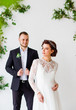 © Yuliia - Elegant couple standing in a white studio with a green leaf décor