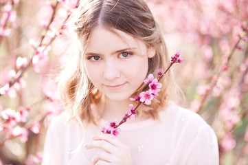 Canvas Print - Smiling girl holding flowers in peach orchard. Looking at camera. Spring time.