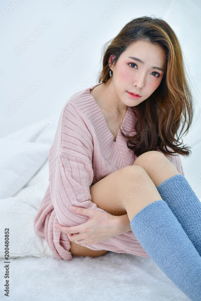 Winter Concept. Cute Asian girl in winter dress. Beautiful woman is  relaxing in a white bedroom. Beautiful women in winter clothes are relaxing  in the morning. Stock-foto | Adobe Stock
