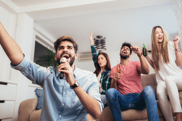 Wall Mural - Group of friends playing karaoke at home. Concept about friendship, home entertainment and people