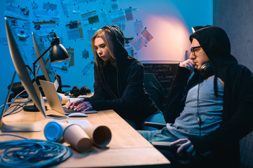 Wall Mural - couple of young hackers using laptop at workplace in dark room