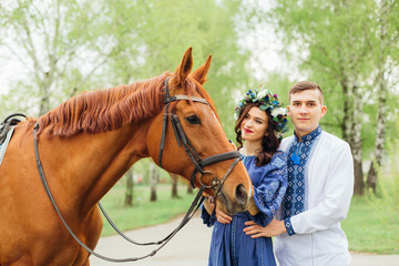 the profile of a beautiful horse and the girl who looks at him and holds him for a bridle. the girl stands near a guy who hugs her waist and looks at the camera lens