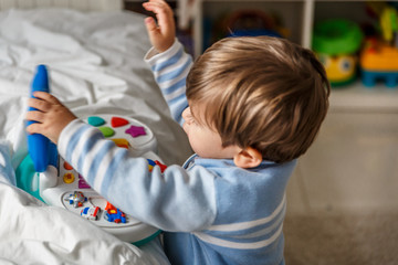 A blond little boy enjoys in his room playing with a musical toy