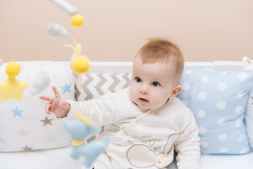 Poster - Cute baby sitting in a white round bed. Light nursery for young children.  Toys for infant cot. Smiling child playing with mobile of felt in sunny bedroom.