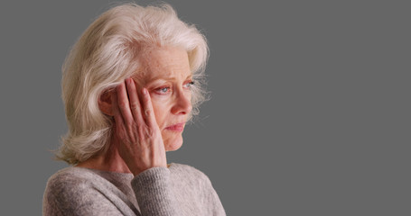 Close-up of sad looking elder woman on gray background touching her temples