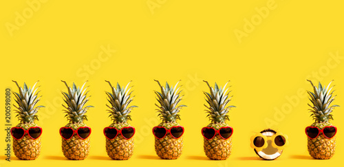 Fotografie, Obraz Series of pineapples and a coconut wearing sunglasses on a yellow background