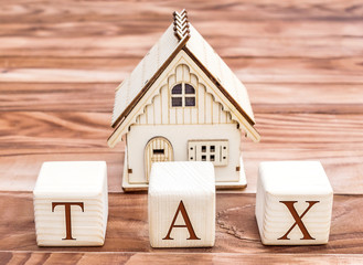 Wooden cubes with word tax and model of house on the wooden background. Property tax concept.